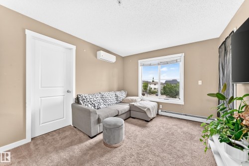 Wall-mounted climate control unit, large picture window, white trim, paneled interior door, and neutral-toned carpeting - #306 5370 Chappelle Rd Sw, Edmonton, AB 