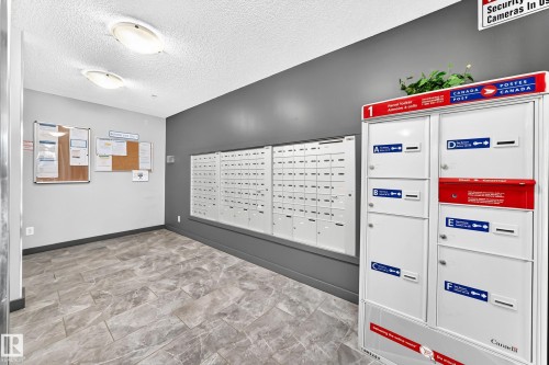 Modern leasing office featuring organized mail sorting stations with multiple compartments, neutral gray accent walls, recessed ceiling lighting, and wood-finish flooring throughout the space - #306 5370 Chappelle Rd Sw, Edmonton, AB 