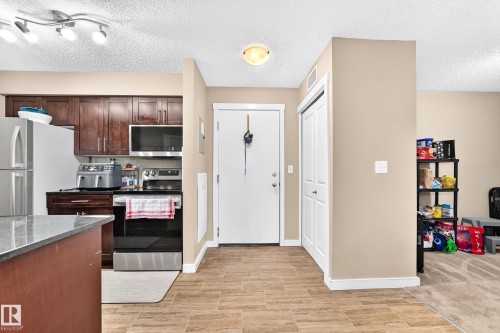 Kitchen featuring dark wood-finish cabinetry, stainless steel appliances, and a gray countertop on the island - #306 5370 Chappelle Rd Sw, Edmonton, AB 