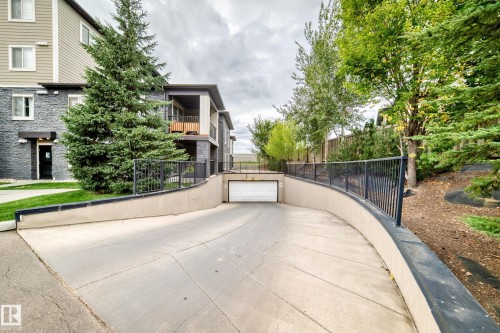 Concrete driveway leading to an integrated garage, featuring a black metal railing - #306 5370 Chappelle Rd Sw, Edmonton, AB 