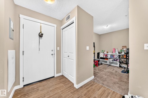 Wood-finish flooring with a white entry door, bi-fold closet doors, and neutral wall paint - #306 5370 Chappelle Rd Sw, Edmonton, AB 