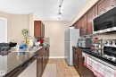Kitchen featuring wood-finish cabinetry, dark countertops, stainless steel appliances, and track lighting - #306 5370 Chappelle Rd Sw, Edmonton, AB 