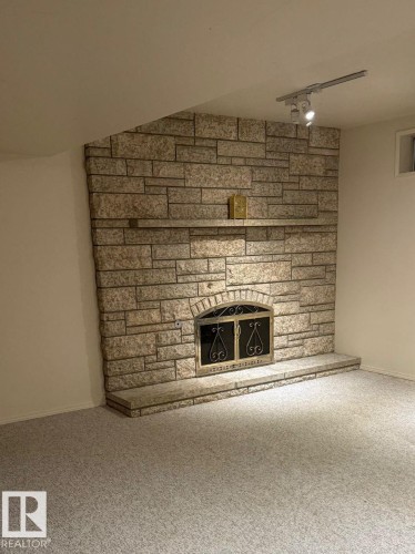Stone-clad fireplace with an ornate iron screen, a stone hearth, and a mantel shelf - 29 Lindbergh Crescent, St. Albert, AB 