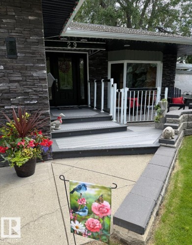 Stone veneer exterior detailing a covered front entry with a dark-framed glass door, composite decking, and a bay window - 29 Lindbergh Crescent, St. Albert, AB 