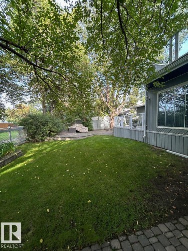 Expansive green lawn, elevated wood-finish deck with glass railing, paved patio area, and mature trees - 29 Lindbergh Crescent, St. Albert, AB 