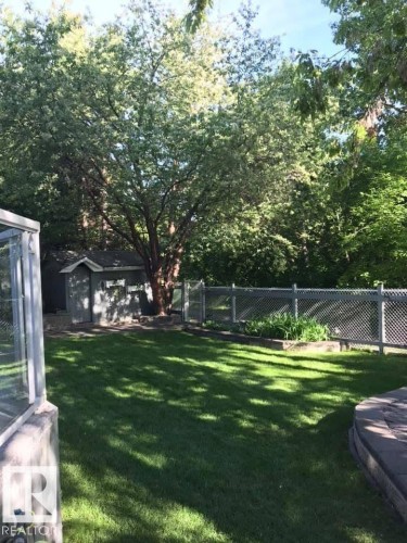 Expansive lawn area with a stone-edged patio and mature trees - 29 Lindbergh Crescent, St. Albert, AB 