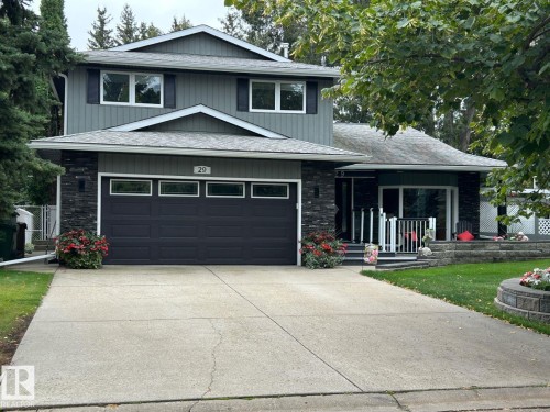 Two-story exterior with horizontal siding, stone veneer accents, an attached two-car garage with transom windows, a concrete driveway, and a front patio with railings - 29 Lindbergh Crescent, St. Albert, AB 