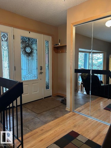 Entryway featuring a white door with decorative glass inserts, ceramic tile flooring, wood-finish flooring, and a mirrored closet door - 29 Lindbergh Crescent, St. Albert, AB 