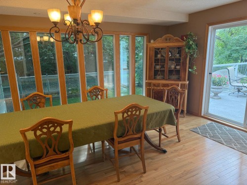 Spacious dining area featuring wood-finish flooring, a decorative chandelier, and an expansive window wall - 29 Lindbergh Crescent, St. Albert, AB 