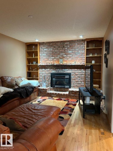Brick fireplace with hearth, built-in shelving, wood-finish flooring, and recessed lighting - 29 Lindbergh Crescent, St. Albert, AB 