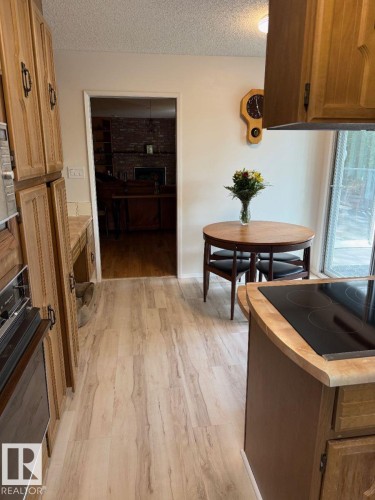 Light wood-finish flooring throughout, wood cabinetry with dark hardware, built-in electric cooktop, and a sliding glass door - 29 Lindbergh Crescent, St. Albert, AB 