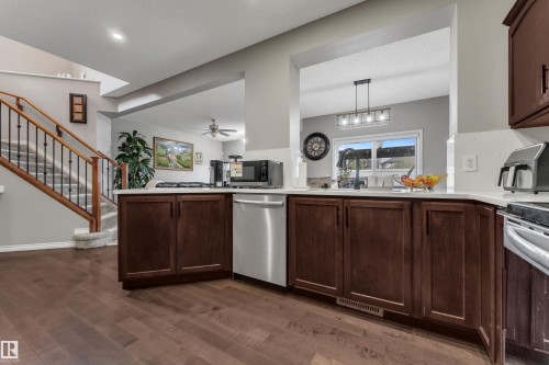 Rich wood-finish flooring, dark wood cabinetry, light countertops, stainless steel dishwasher, and a staircase with wood newel posts and black metal spindles - 3230 21A Avenue Nw, Edmonton, AB 