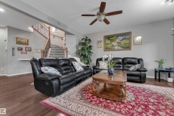 Wood-finish flooring, staircase with wood handrails, ceiling fan with integrated lighting, and neutral wall paint - 