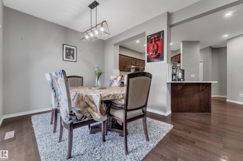 Open-concept dining area featuring wood-finish flooring, a modern chandelier, a pass-through window to the kitchen, and a built-in counter with storage - 3230 21A Avenue Nw, Edmonton, AB 