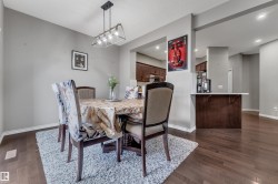 Open-concept dining area featuring wood-finish flooring, a modern chandelier, a pass-through window to the kitchen, and a built-in counter with storage - 