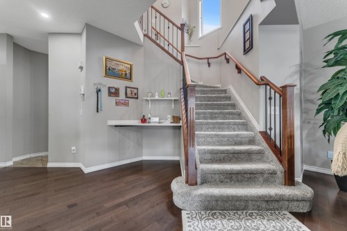 Carpeted staircase with wood-finish handrails and wrought iron balusters, wood-finish flooring, and a built-in wall shelf - 3230 21A Avenue Nw, Edmonton, AB 