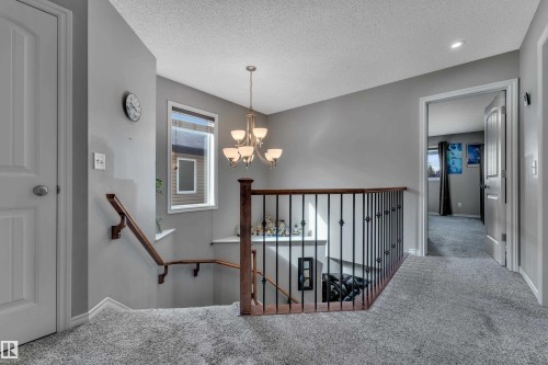 Upper-level landing with gray carpet flooring and walls, featuring a wrought iron and wood banister - 3230 21A Avenue Nw, Edmonton, AB 