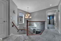 Upper-level landing with gray carpet flooring and walls, featuring a wrought iron and wood banister - 