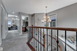 Carpeted hallway with a chandelier, open staircase featuring wrought iron balusters, and a built-in vanity with wood-finish cabinetry - 
