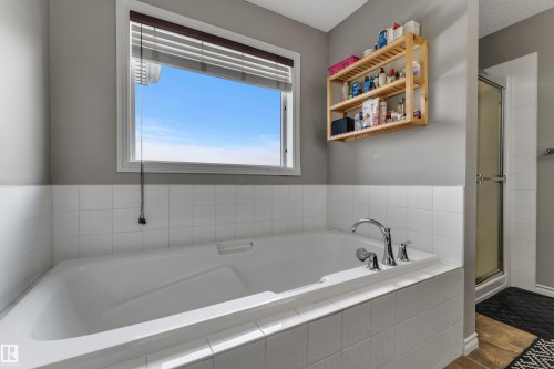 Built-in bathtub with white tile surround, chrome fixtures, and an adjacent enclosed shower - 3230 21A Avenue Nw, Edmonton, AB 