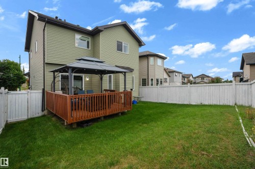 Expansive backyard featuring a manicured lawn, a wood-finish deck with a gazebo, and a white privacy fence - 3230 21A Avenue Nw, Edmonton, AB 