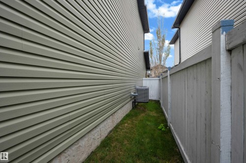 Exterior siding and foundation with a partial fence, air conditioning unit, and a grassy area - 3230 21A Avenue Nw, Edmonton, AB 