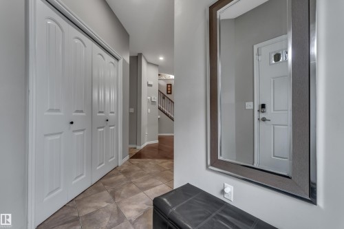 Tile flooring, white bi-fold closet doors, wall-mounted mirror, white entry door with smart lock, and wood-finish flooring in the background - 3230 21A Avenue Nw, Edmonton, AB 