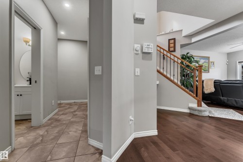 Wood-finish flooring, staircase with wood handrail and wrought iron spindles, recessed lighting, and a vanity with a circular mirror and under-sink cabinetry - 3230 21A Avenue Nw, Edmonton, AB 