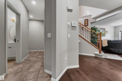 Wood-finish flooring, staircase with wood handrail and wrought iron spindles, recessed lighting, and a vanity with a circular mirror and under-sink cabinetry - 