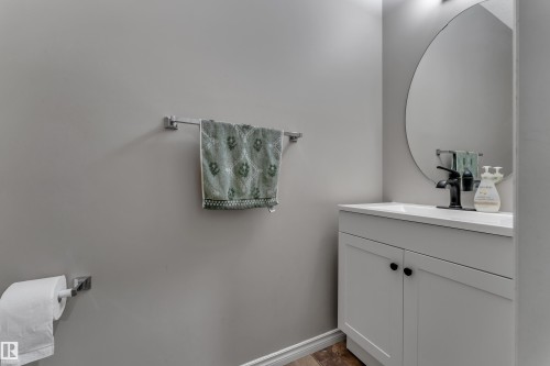 White vanity with matte black hardware, integrated rectangular sink, and a circular wall mirror - 3230 21A Avenue Nw, Edmonton, AB 