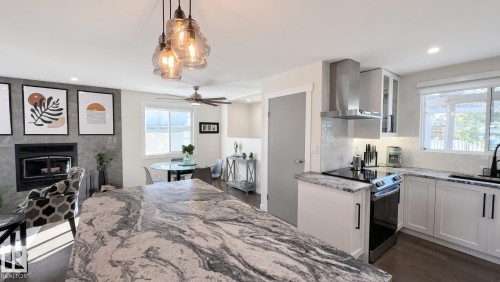 Kitchen featuring a large island with a patterned countertop, white cabinetry, a built-in oven with a range hood, and a tile backsplash - 3508 106A Street Nw, Edmonton, AB 
