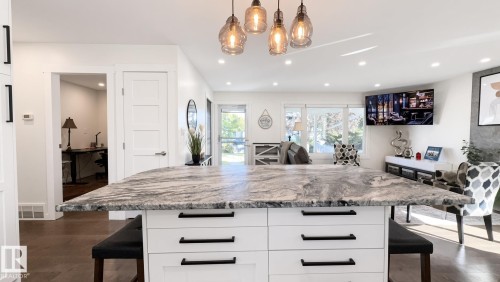 Kitchen island with a natural stone countertop, white cabinetry with black hardware, and pendant lighting - 3508 106A Street Nw, Edmonton, AB 