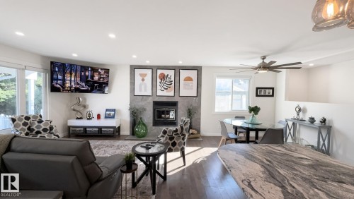 Open-concept living area with wood-finish flooring, a contemporary fireplace, recessed lighting, and a large window - 3508 106A Street Nw, Edmonton, AB 