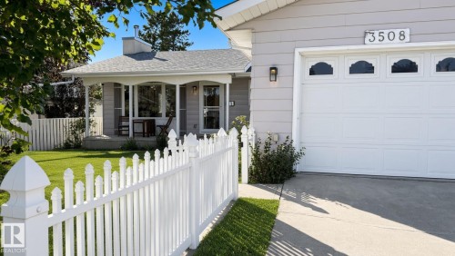White picket fence, covered front porch, light gray exterior siding, attached garage with decorative windows, and concrete driveway - 3508 106A Street Nw, Edmonton, AB 