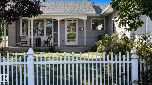 Front exterior featuring a white picket fence, covered front porch, bay window with shutters, and gray horizontal siding - 3508 106A Street Nw, Edmonton, AB 