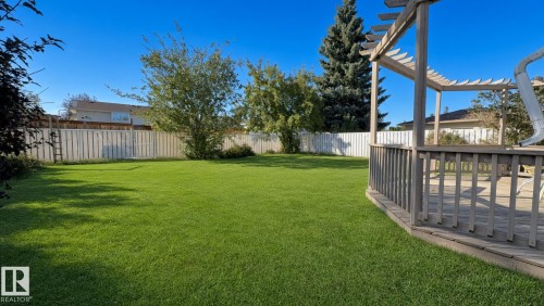 Expansive backyard with a large lawn area, wooden privacy fencing, mature trees, and a spacious wooden deck featuring a pergola structure - 3508 106A Street Nw, Edmonton, AB 