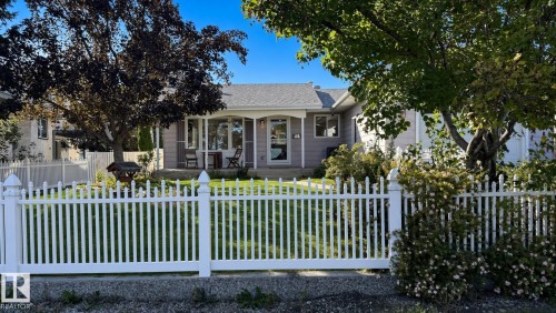 Ranch-style exterior with a covered front porch, white picket fence, mature trees, and a landscaped front yard - 3508 106A Street Nw, Edmonton, AB 
