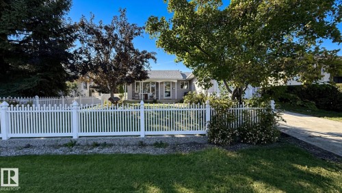 Front yard featuring a white picket fence, mature trees, and a concrete driveway - 3508 106A Street Nw, Edmonton, AB 