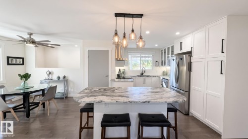 Gourmet kitchen featuring a large kitchen island with counter seating, stainless steel appliances, white cabinetry, and wood-finish flooring - 3508 106A Street Nw, Edmonton, AB 