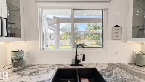Kitchen sink with a black matte faucet, white subway tile backsplash, and patterned stone-finish countertops - 3508 106A Street Nw, Edmonton, AB 