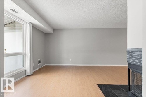 Wood-finish flooring, light grey wall paint, and a fireplace with grey stacked stone surround - #4 14620 26 St Nw, Edmonton, AB 