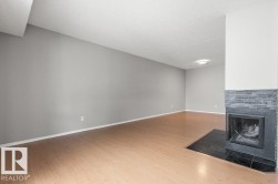 Spacious room featuring wood-finish flooring, light grey wall paint, and a fireplace with a dark tile surround and hearth - 