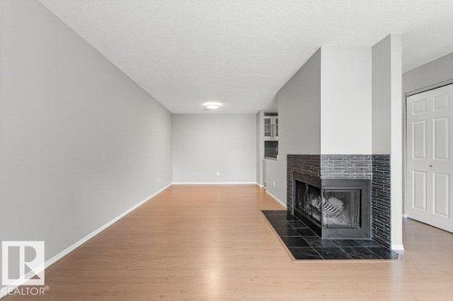 Living area featuring wood-finish flooring, a corner fireplace with a dark tile surround, and light gray painted walls - #4 14620 26 St Nw, Edmonton, AB 