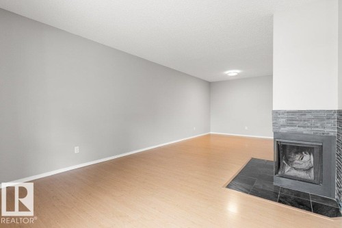 Wood-finish flooring with a corner fireplace featuring stacked stone and a dark tile hearth - #4 14620 26 St Nw, Edmonton, AB 