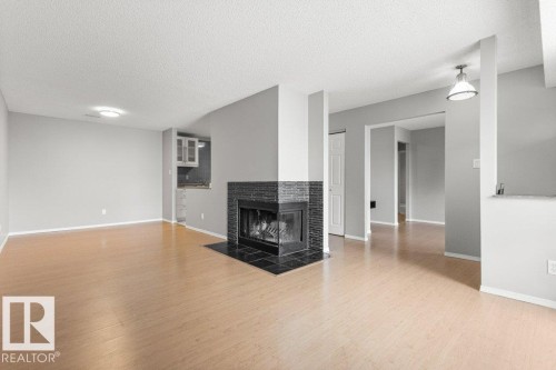 Wood-finish flooring, a black-tiled fireplace, recessed lighting, and a kitchen area with upper cabinetry - #4 14620 26 St Nw, Edmonton, AB 