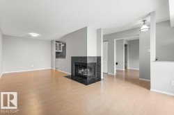 Wood-finish flooring, a black-tiled fireplace, recessed lighting, and a kitchen area with upper cabinetry - 