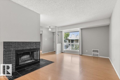 Wood-finish flooring, a fireplace with a black tile surround, a large window, and a built-in wall heater - #4 14620 26 St Nw, Edmonton, AB 