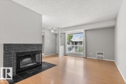 Wood-finish flooring, a fireplace with a black tile surround, a large window, and a built-in wall heater - 