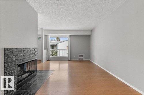Living area featuring wood-finish flooring, a stacked stone fireplace with a tile hearth, and a balcony with white railings - #4 14620 26 St Nw, Edmonton, AB 