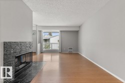 Living area featuring wood-finish flooring, a stacked stone fireplace with a tile hearth, and a balcony with white railings - 